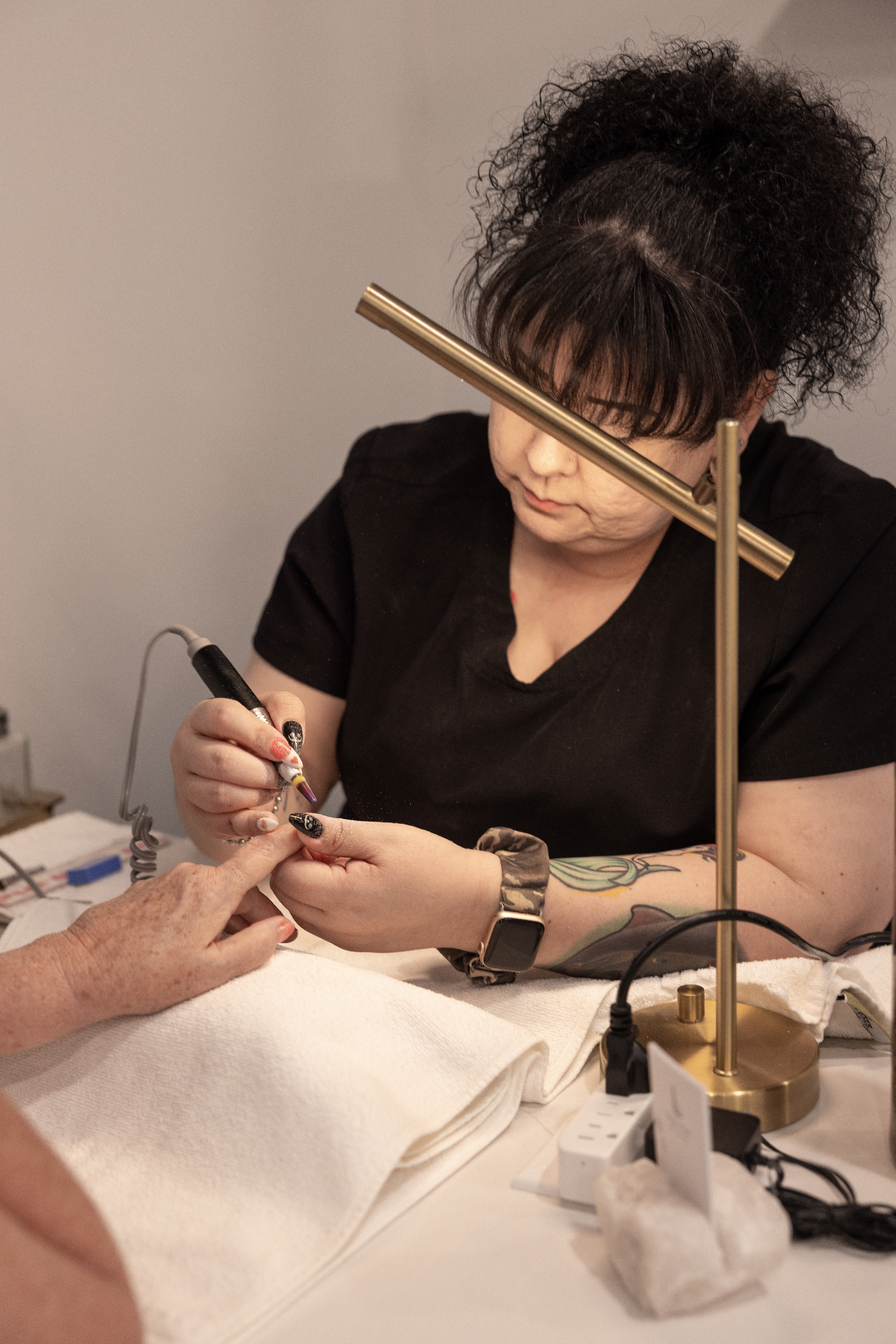 Nail technician working on a client's nails under a lamp